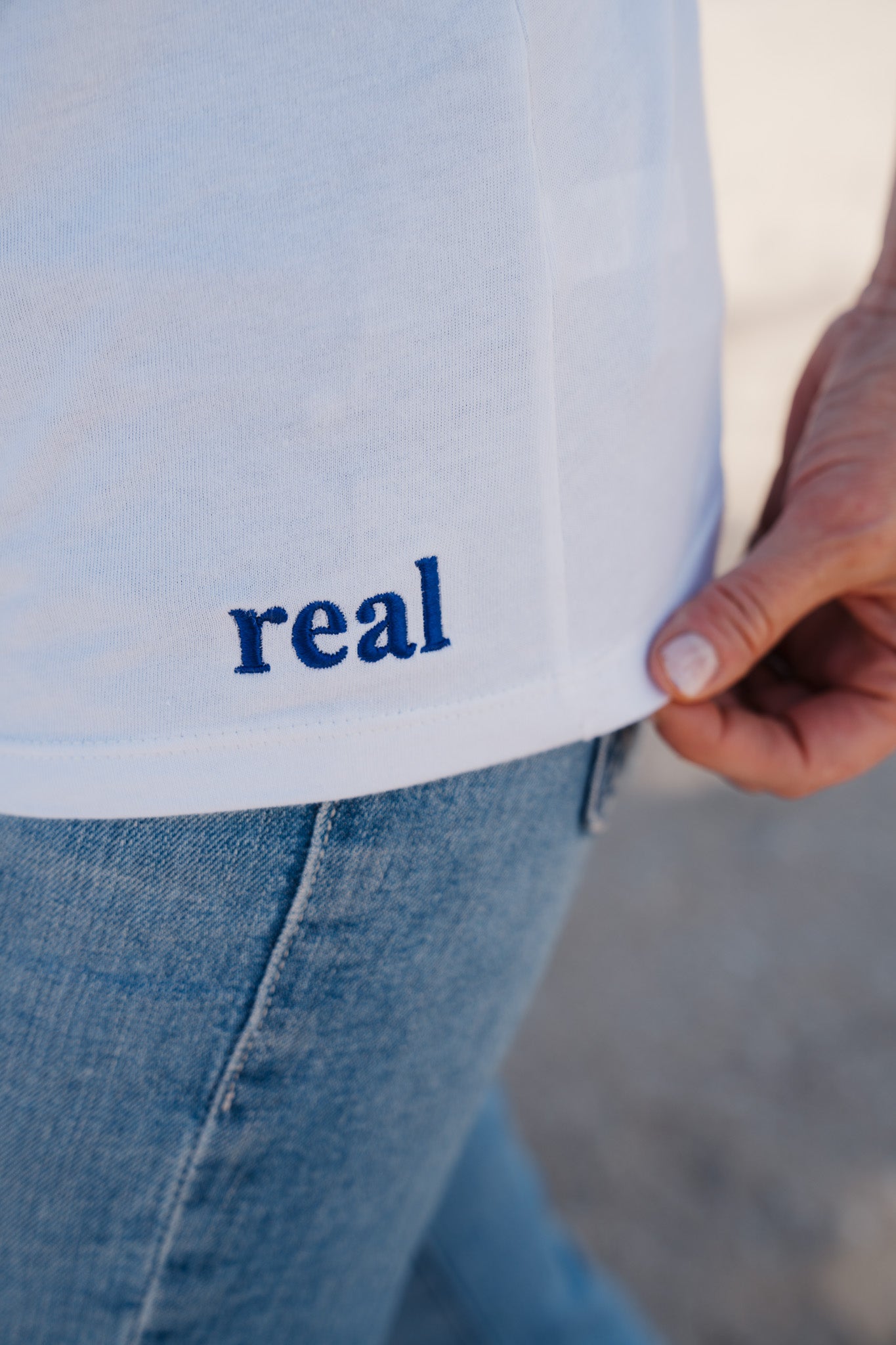 Women's White Tee with dark purple "real" embroidered on the left hip area | RaileyReal