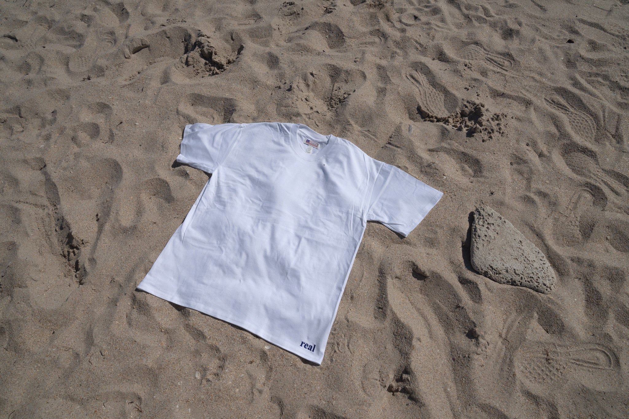 Women's White Tee with dark purple "real" embroidered on the left hip area | RaileyReal