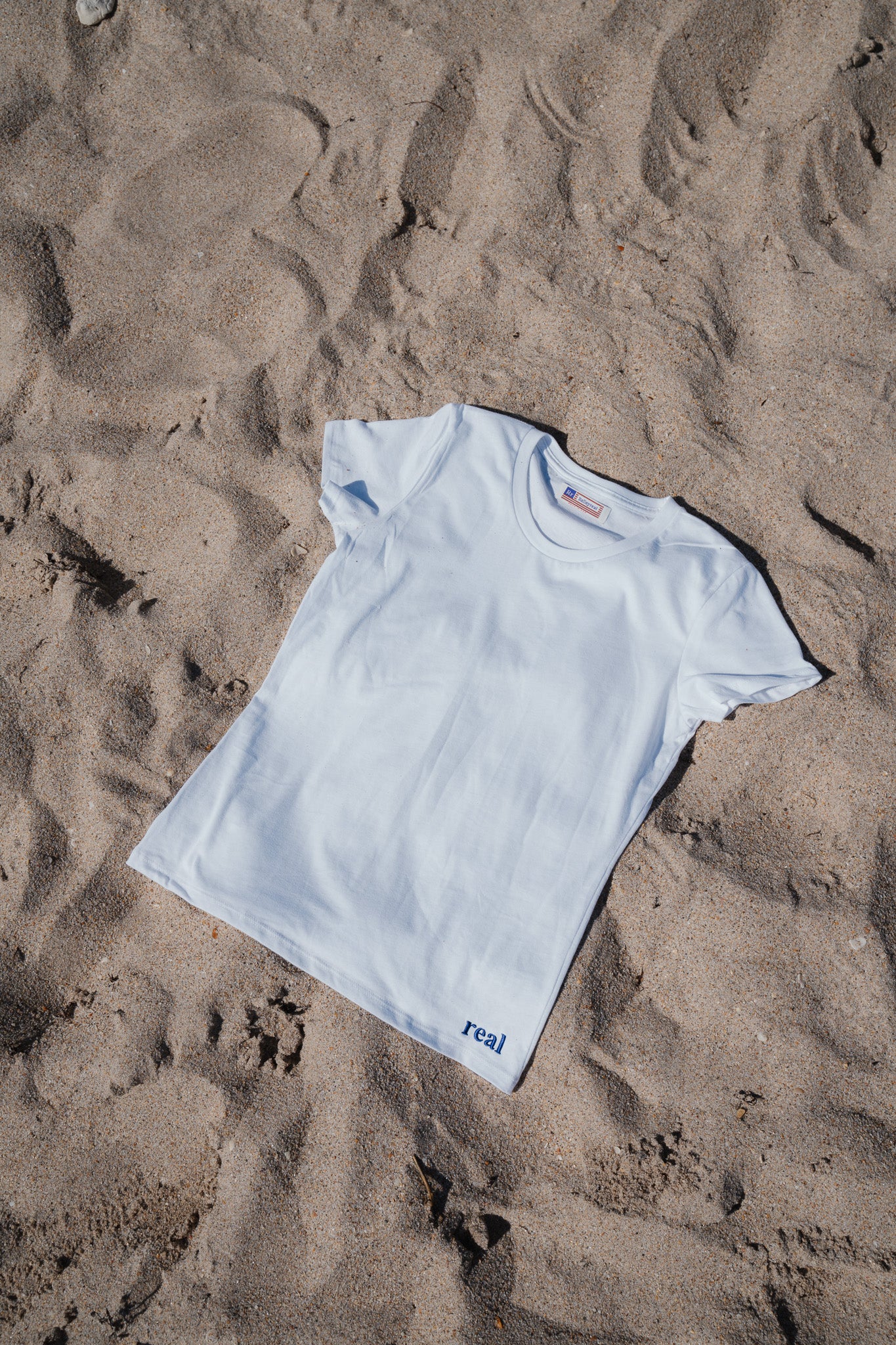 Women's White Tee with dark purple "real" embroidered on the left hip area | RaileyReal